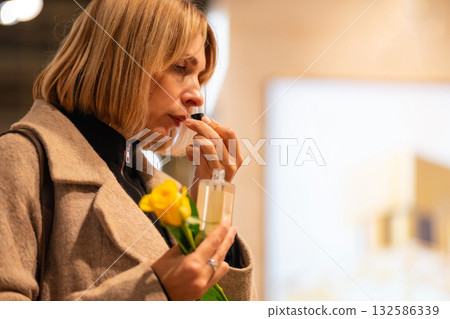 A woman in a beige coat examining a bottle of perfume A woman in a beige coat examining a bottle of perfume 132586339
