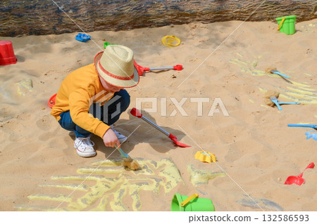 Good leisure for a child. Teaching a child through play. A handsome boy 3 oldl in a yellow jacket excavates the remains of dinosaurs. High quality photo. 132586593