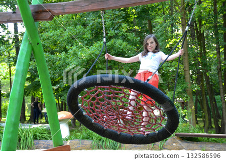 Close up happy little child girl play and sitting on the swing in the nature park. Teen girl on a swing in the summer park. High quality photo 132586596