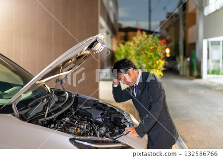 A man in a suit checks a car's malfunction on the road at night. He opens the hood of his car and looks helpless. 132586766