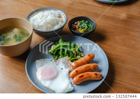 A Japanese-Western breakfast of sausages, fried eggs, stir-fried green peppers and natto 132587444