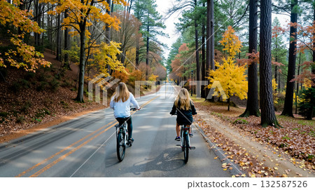 Two girls riding bikes down a road in the woods 132587526