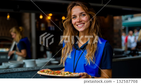 A woman holding a pizza in a restaurant kitchen A woman holding a pizza in a restaurant kitchen 132587708