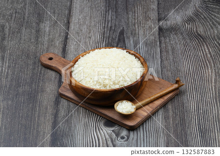 Raw white rice on black background. Long uncooked rice in wooden plate. Natural organic food. Traditional Asian cereal culture. Raw white rice on black background. Long uncooked rice in wooden plate. Natural organic food. Traditional Asian cereal culture. 132587883