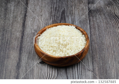 Raw white rice on black background. Long uncooked rice in wooden plate. Natural organic food. Traditional Asian cereal culture. Raw white rice on black background. Long uncooked rice in wooden plate. Natural organic food. Traditional Asian cereal culture. 132587885