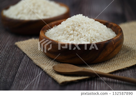 Raw white rice on wooden background. Long uncooked rice in wooden plate. Natural organic food. Traditional Asian cereal culture. Raw white rice on wooden background. Long uncooked rice in wooden plate. Natural organic food. Traditional Asian cereal culture. 132587890