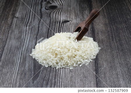 Raw white rice on wooden background. Long uncooked rice in wooden plate. Natural organic food. Traditional Asian cereal culture. Raw white rice on wooden background. Long uncooked rice in wooden plate. Natural organic food. Traditional Asian cereal culture. 132587909