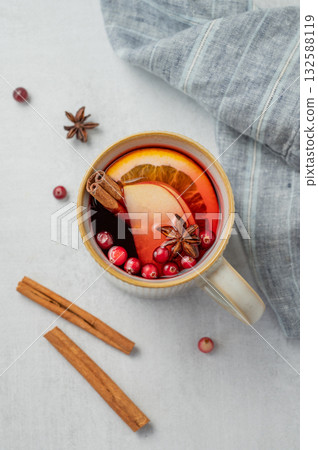 A hot cranberry Christmas drink in a mug on a light background with cinnamon and napkin. A hot cranberry Christmas drink in a mug on a light background with cinnamon and napkin. 132588119