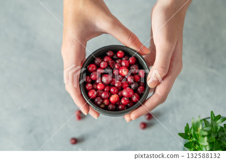 Hand holding bowl of fresh cranberries on a light table with green branch. Hand holding bowl of fresh cranberries on a light table with green branch. 132588132