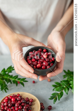 Hand holding bowl of fresh cranberries on a light table with green branch. Hand holding bowl of fresh cranberries on a light table with green branch. 132588133