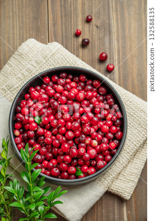 Fresh cranberries in a dark bowl on a wooden background with green branch and napkin. Fresh cranberries in a dark bowl on a wooden background with green branch and napkin. 132588135