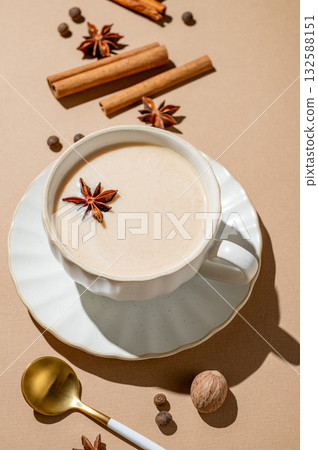 Traditional Indian masala chai tea with milk and spices in a cup on a beige background with cinnamon 132588151