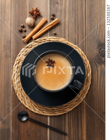 Traditional Indian masala chai tea with milk and spices in a black cup on a dark wooden background Traditional Indian masala chai tea with milk and spices in a black cup on a dark wooden background 132588167
