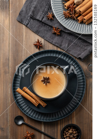 Traditional Indian masala chai tea with milk and spices in a black cup on a dark wooden background 132588169