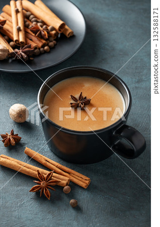 Traditional Indian masala chai tea with milk and spices in a black cup on a dark background. Traditional Indian masala chai tea with milk and spices in a black cup on a dark background. 132588171