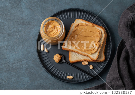 Peanut butter toast on a black plate on a dark background with nuts, napkin and spoon. 132588187