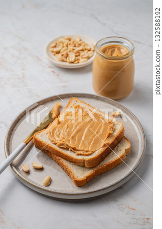 Peanut butter toast on a plate on a light marble background with nuts and knife. 132588192