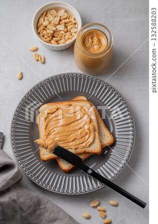 Peanut butter toast on a dark plate on a light background with nuts, napkin and knife 132588203