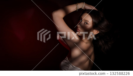 Young woman posing with shadows projected on her body in studio with red background Young woman posing with shadows projected on her body in studio with red background 132588226
