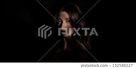 Mysterious young woman emerging from darkness with a captivating gaze 132588227