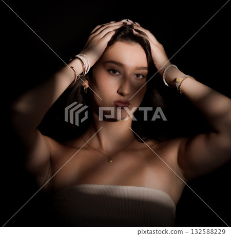 Young woman holding her hair with light and shadow creating an artistic effect Young woman holding her hair with light and shadow creating an artistic effect 132588229