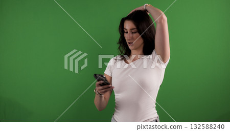 Young woman holding smartphone and posing on green screen background 132588240