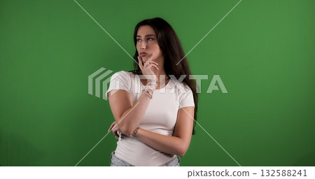 Young woman thinking with hand on chin against green screen background 132588241