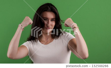 Young woman flexing biceps on green background Young woman flexing biceps on green background 132588266