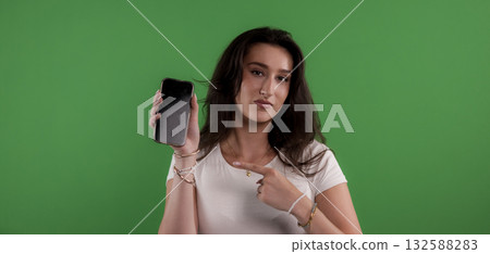 Young woman pointing at smartphone with green screen background Young woman pointing at smartphone with green screen background 132588283