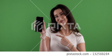 Young woman pointing at smartphone with blank screen on green background Young woman pointing at smartphone with blank screen on green background 132588284