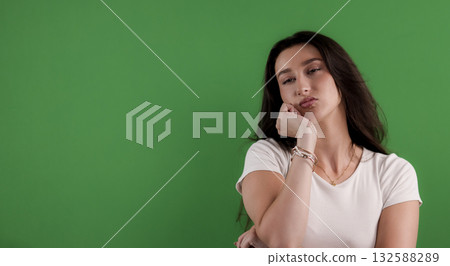 Young woman with bored expression resting face on hand against green background Young woman with bored expression resting face on hand against green background 132588289
