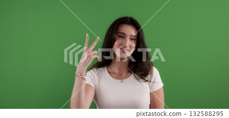 Young woman showing peace sign with fingers on green screen background 132588295