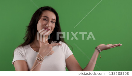 Young woman pointing her finger to her open hand on green screen background Young woman pointing her finger to her open hand on green screen background 132588308