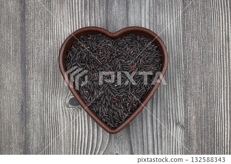 pile of black rice in a wooden bowl on a wooden table close-up 132588343