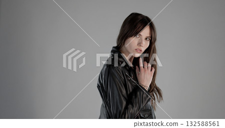 Young woman wearing leather jacket posing on gray background Young woman wearing leather jacket posing on gray background 132588561