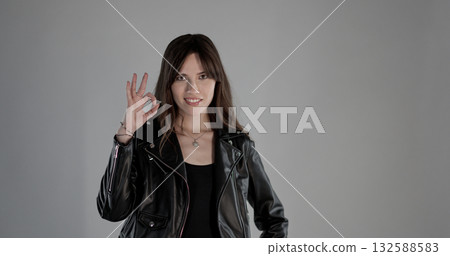 Young woman wearing black leather jacket making ok sign with fingers Young woman wearing black leather jacket making ok sign with fingers 132588583