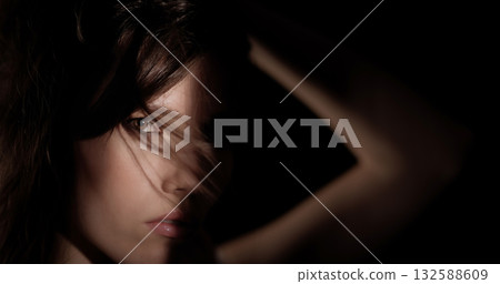 Mysterious woman hiding face with arm and hair in the shadows 132588609