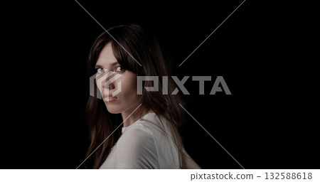 Serious young woman turning head and looking over shoulder on black background 132588618
