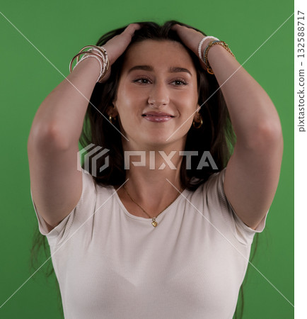 Young woman holding her hair with hands on green background Young woman holding her hair with hands on green background 132588717