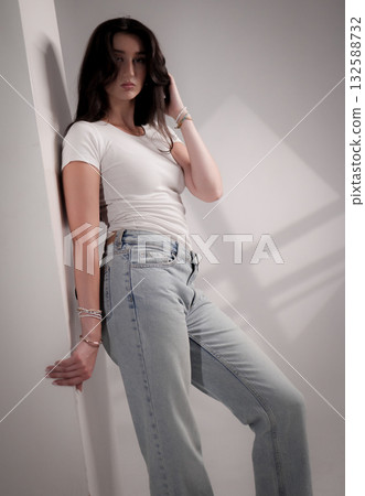 Fashion model posing while leaning against a wall, wearing jeans and t shirt Fashion model posing while leaning against a wall, wearing jeans and t shirt 132588732