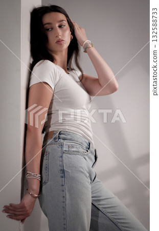 Young woman posing and touching her hair while leaning against a wall 132588733