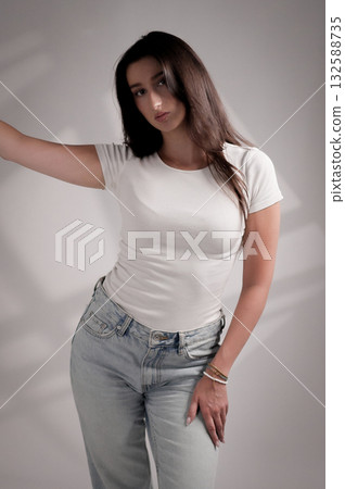 Young woman posing wearing white t shirt and jeans in studio with shadows Young woman posing wearing white t shirt and jeans in studio with shadows 132588735