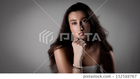 Young woman with hand on chin posing in studio with gray background Young woman with hand on chin posing in studio with gray background 132588767