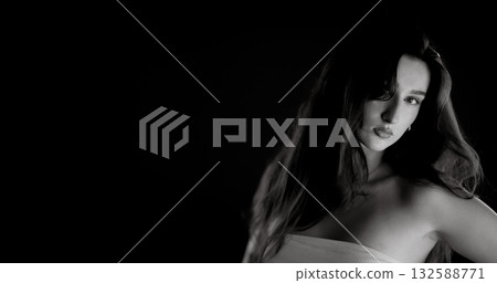 Beautiful young woman with long hair posing in studio on black background, black and white portrait Beautiful young woman with long hair posing in studio on black background, black and white portrait 132588771