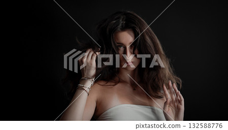 Young woman playing with her long brown hair on black background 132588776