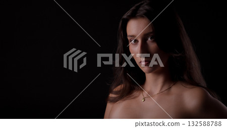 Portrait of young woman with long brown hair posing on black background 132588788
