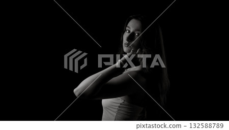 Young woman posing in studio with black background touching her face 132588789