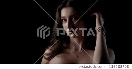 Young woman with long hair touching her head and wearing bracelets and necklace posing on black background Young woman with long hair touching her head and wearing bracelets and necklace posing on black background 132588798