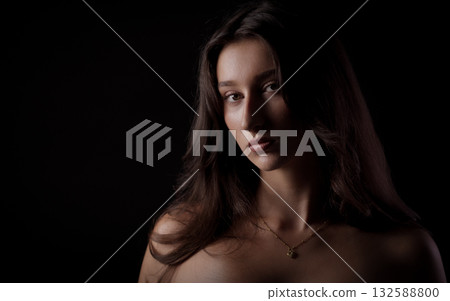 Portrait of young woman with long brown hair posing on black background 132588800
