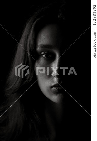 Young woman showing half face emerging from darkness 132588802